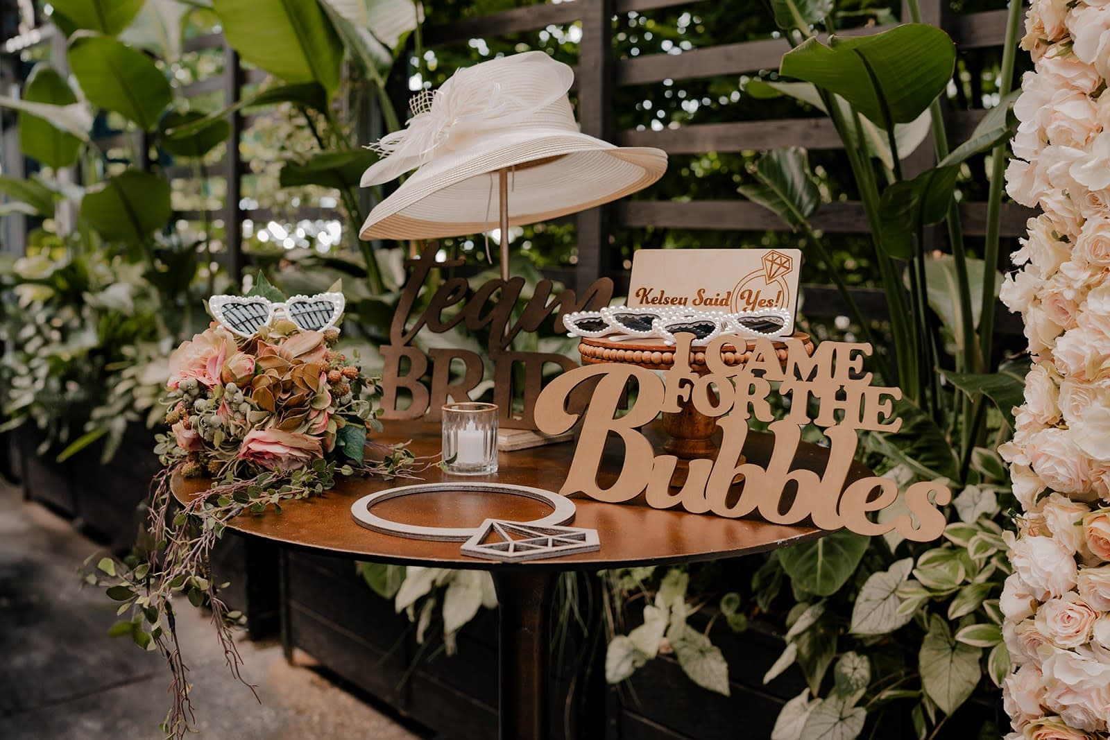 Photo booth props table with a white derby hat, heart sunglasses and a Team Bride sign for a bridal shower